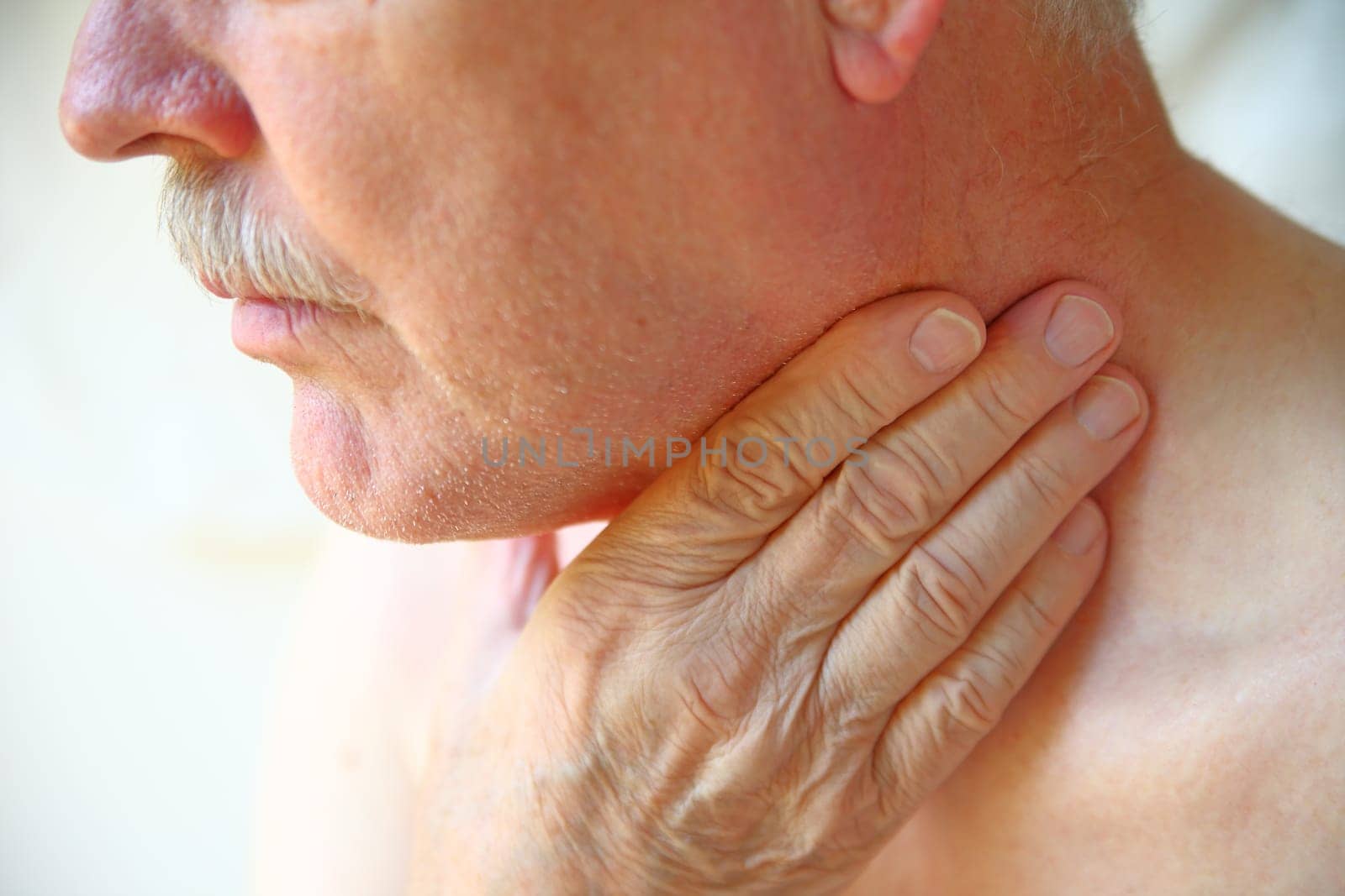 Older man with his hand against his throat, natural light