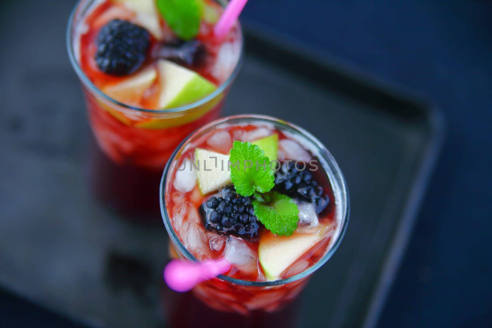 Two wine cocktails with fresh apple, blackberries and mint on ice with a dark tray