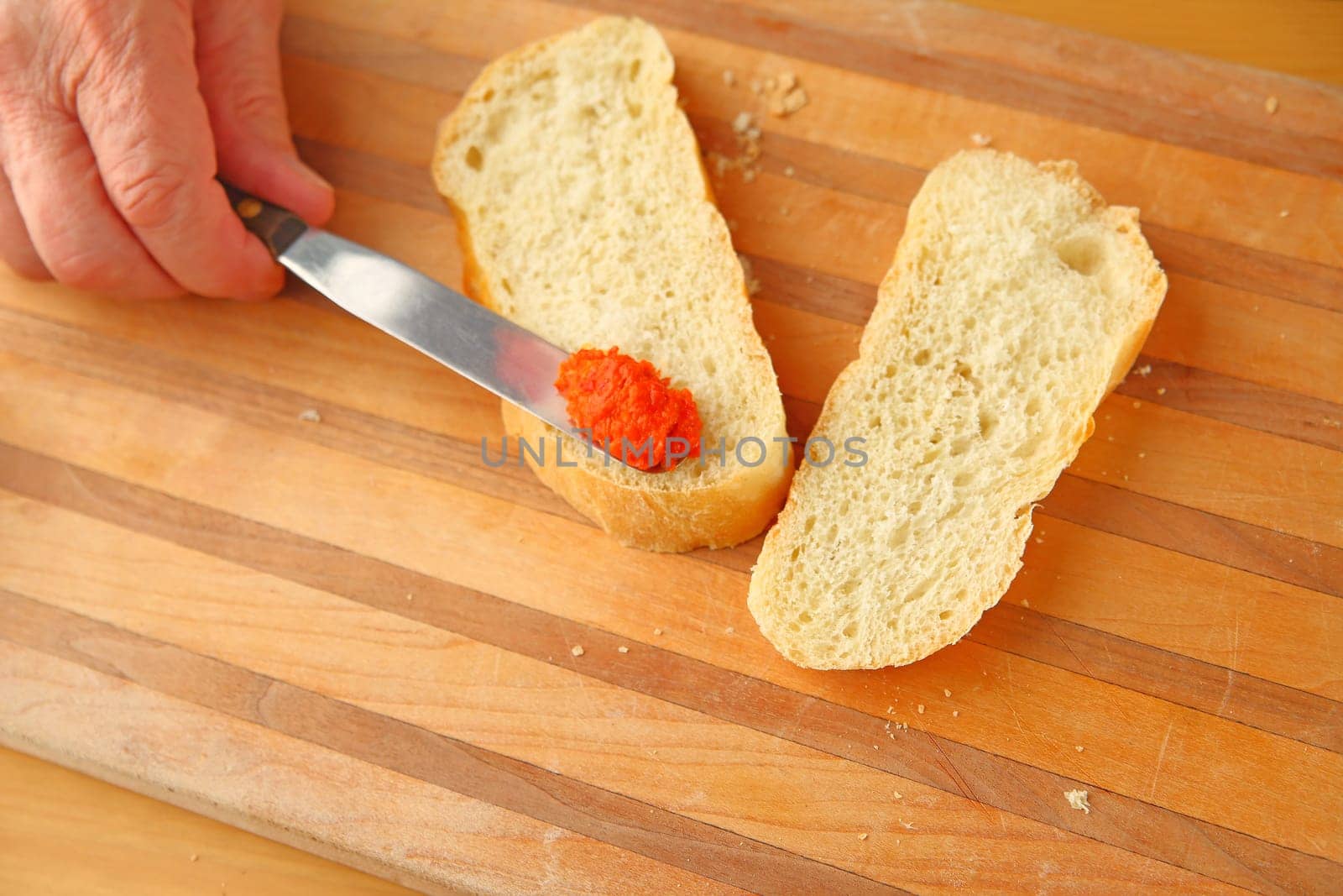 Man spreads bell pepper tapenade on sourdough bread with copy space