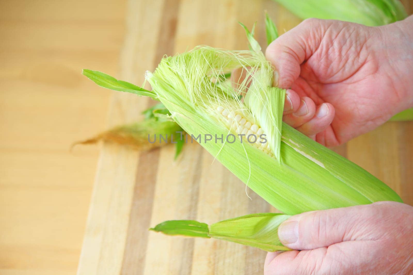A man pulls the husk from an ear of corn over a cutting board