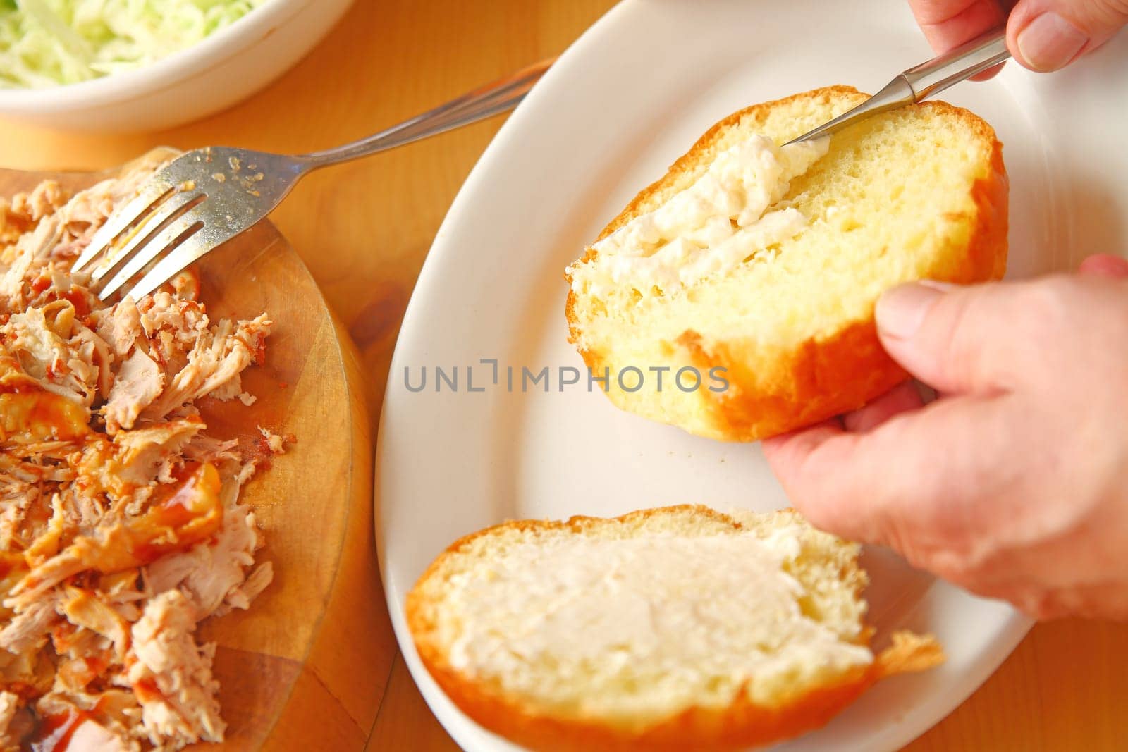 A man puts mayonnaise on brioche buns before adding pulled chicken for a sandwich