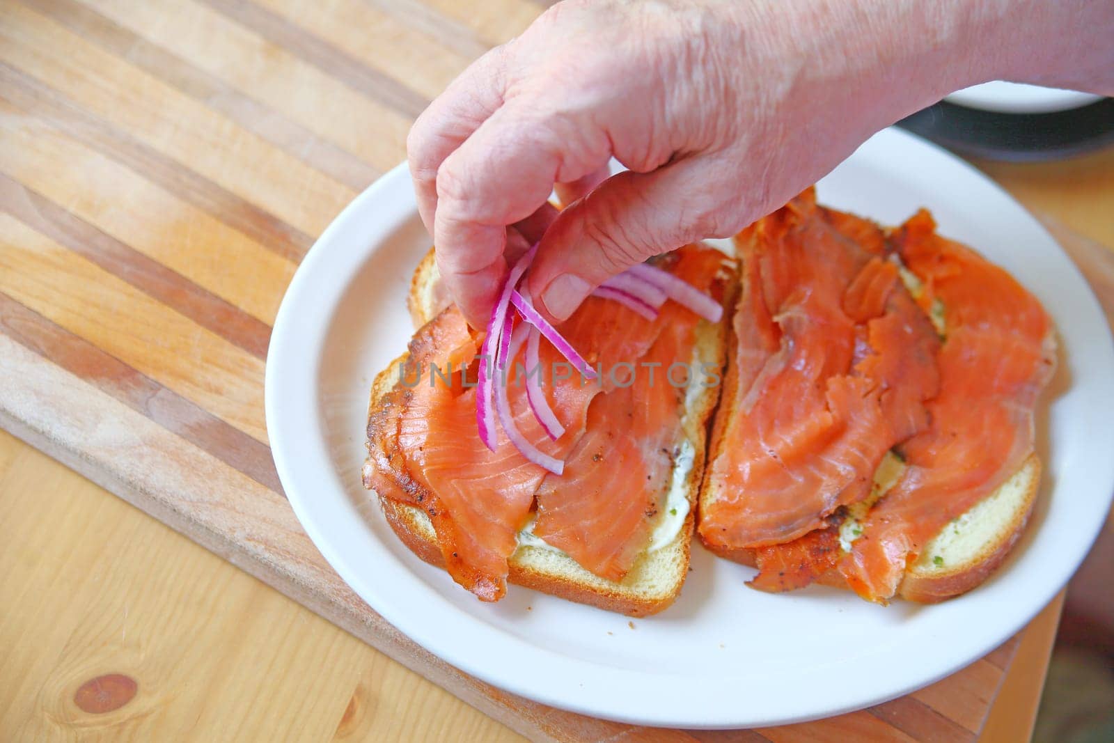 A man puts sliced onions on a salmon sandwich with room for text