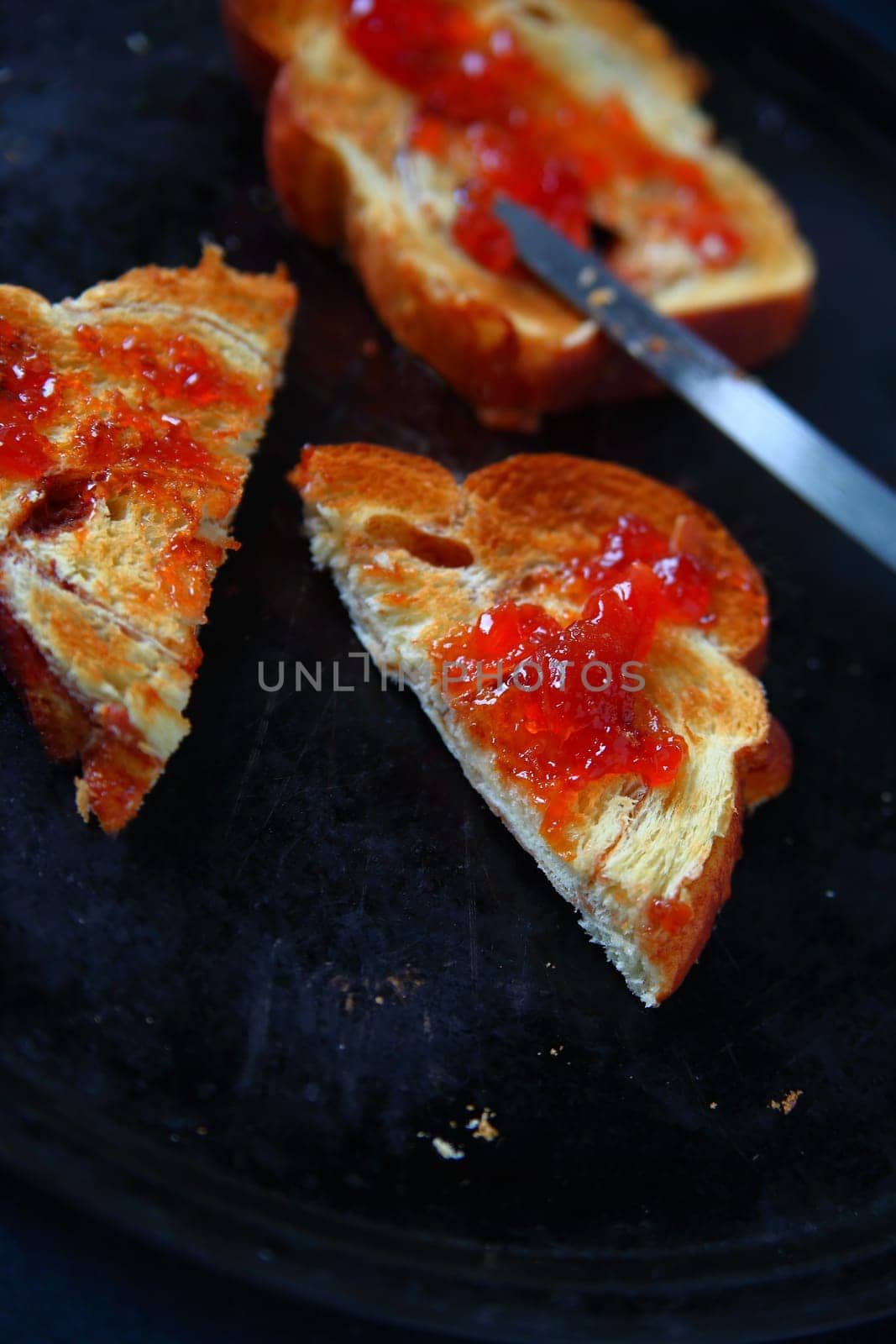 Slices of toast with raspberry jam, one cut in half, on a dark metal baking pan