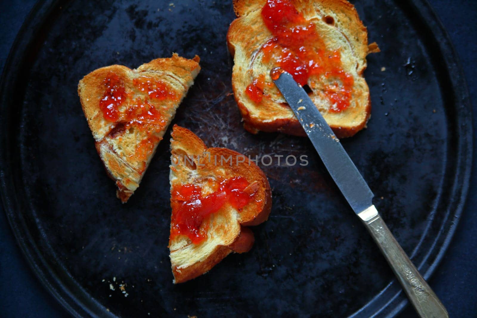 Spreading raspberry jam on toast slices seen from above