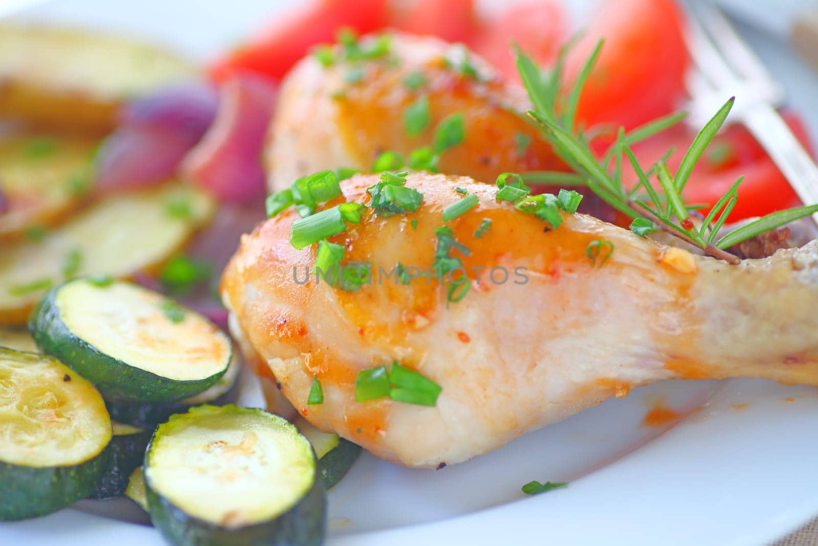 Closeup of roast chicken legs with zucchini, tomatoes, onions, scallions and rosemary