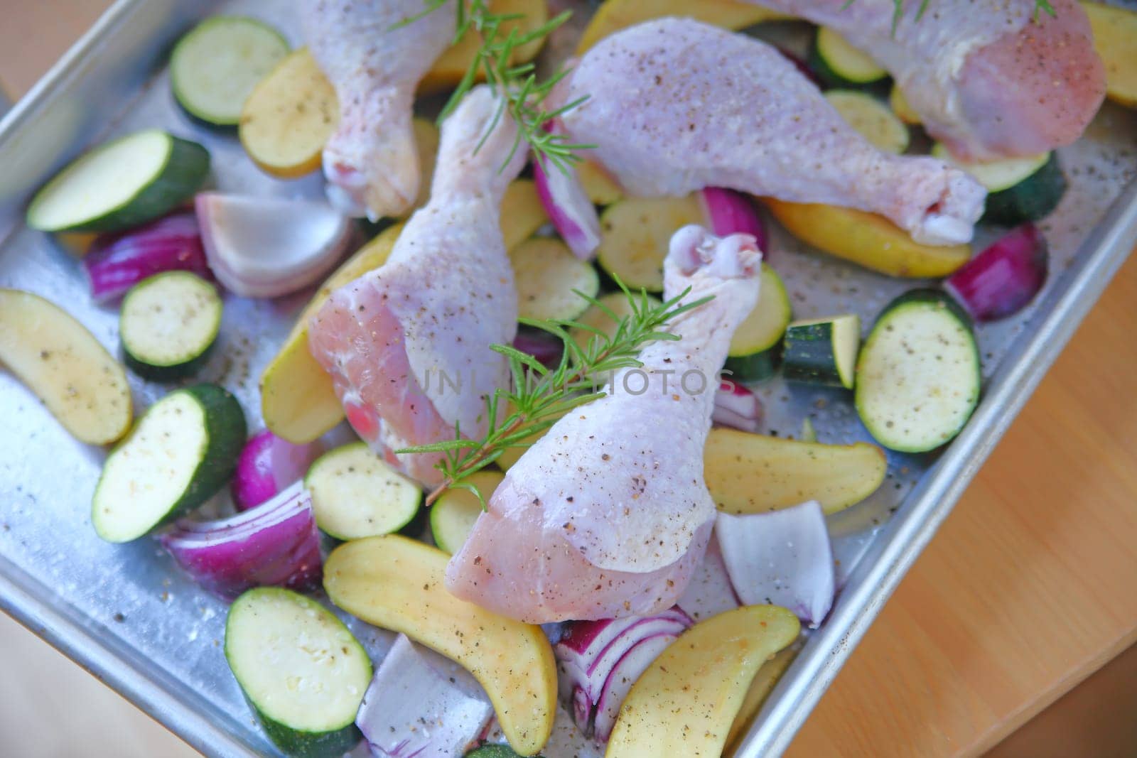Sheet pan dinner of chicken legs, zucchini, fingerling potatoes, onions and rosemary before cooking