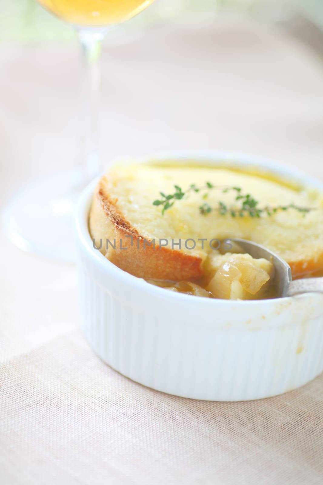 Small bowl of French onion soup with fresh thyme sprigs, a glass of white wine and room for text