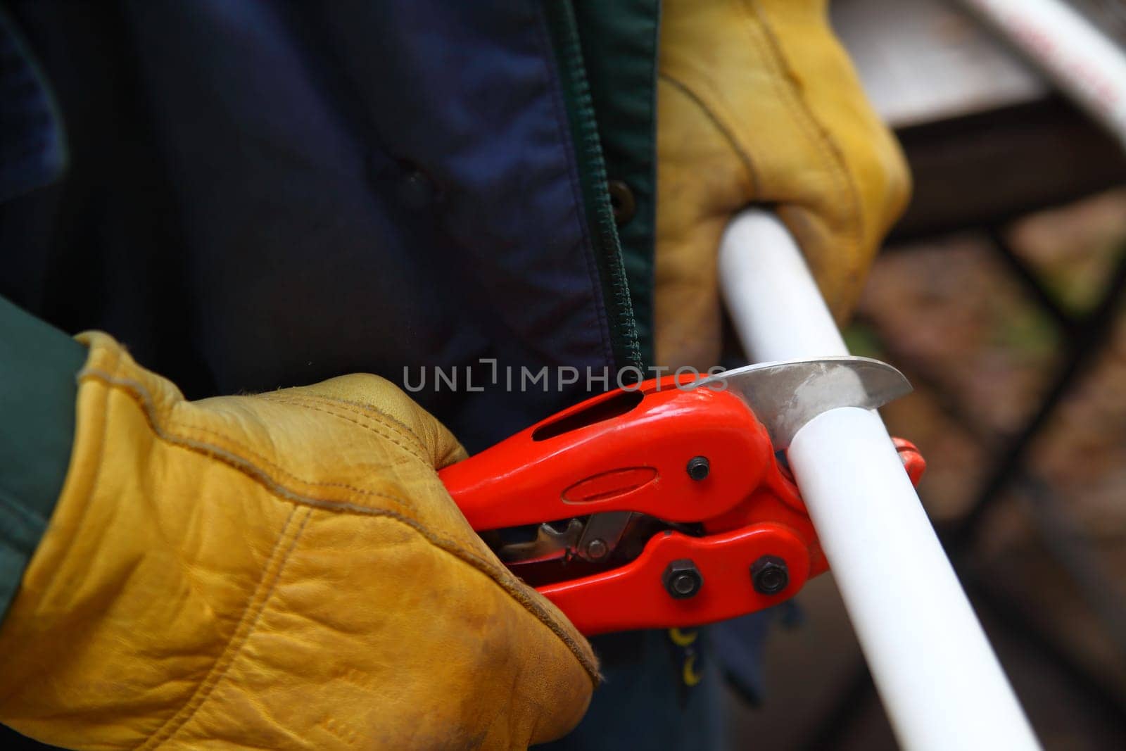 Man with work gloves uses tool to cut a piece of PVC pipe