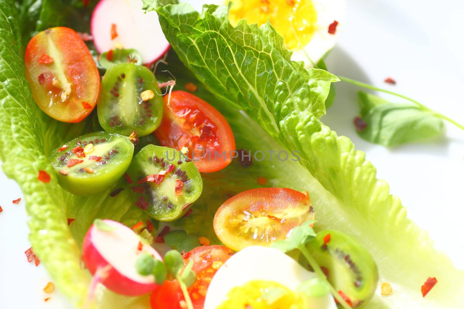 Overhead of lettuce leaves with cherry tomatoes, baby kiwi fruits, radishes and boiled eggs with red pepper flakes