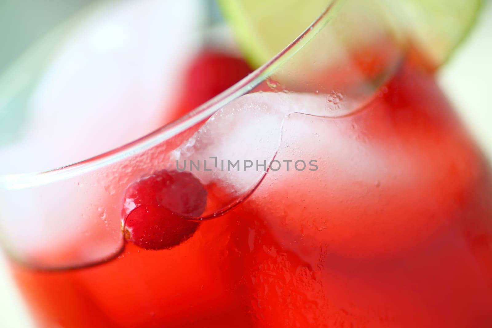 Closeup view of an icy drink made with cranberry juice with fresh berries and a slice of lime