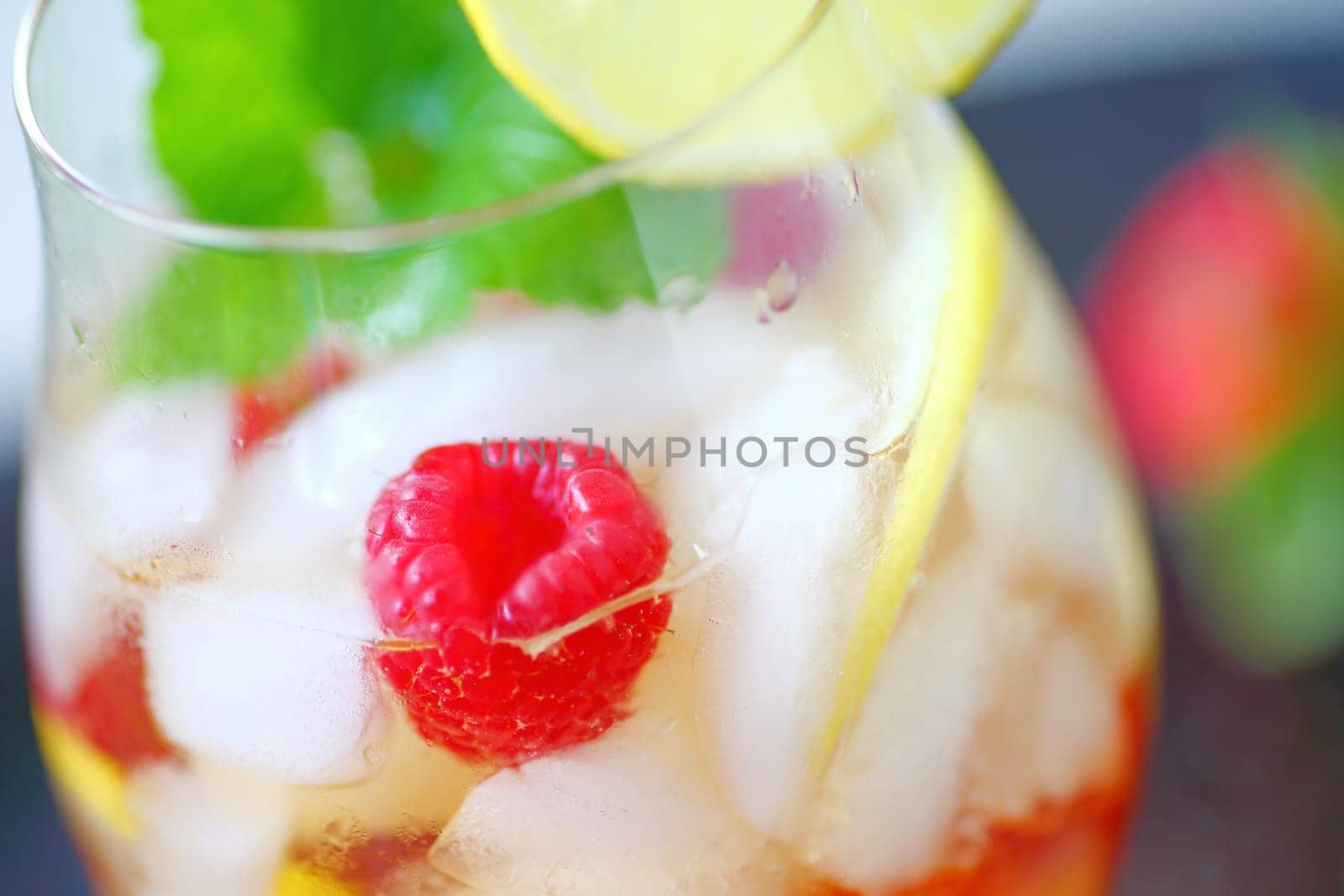 Closeup of cold drink with white wine, lemon, raspberries and mint