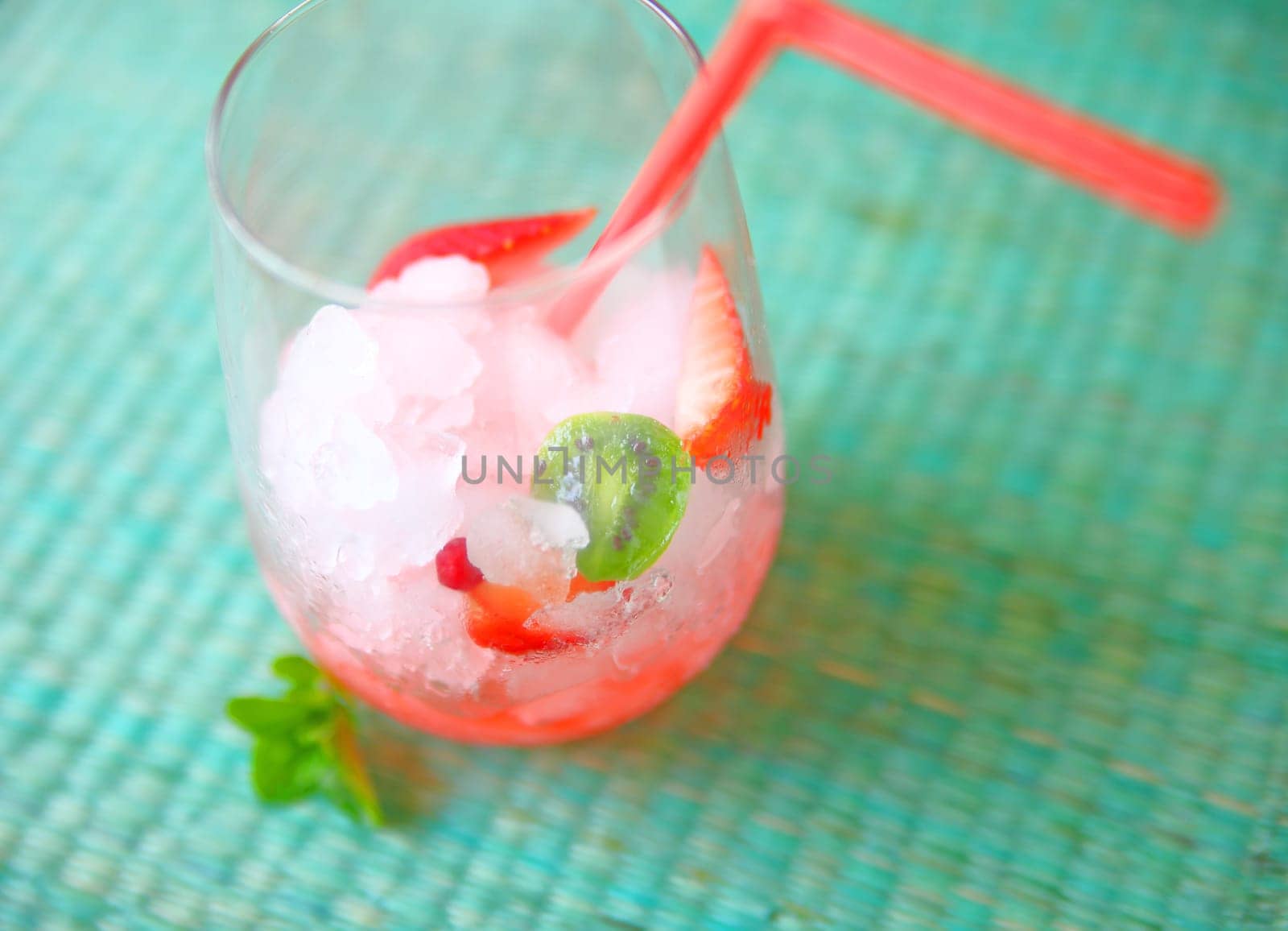 Crushed ice with cut up strawberries and baby kiwifruit with a straw with room for text
