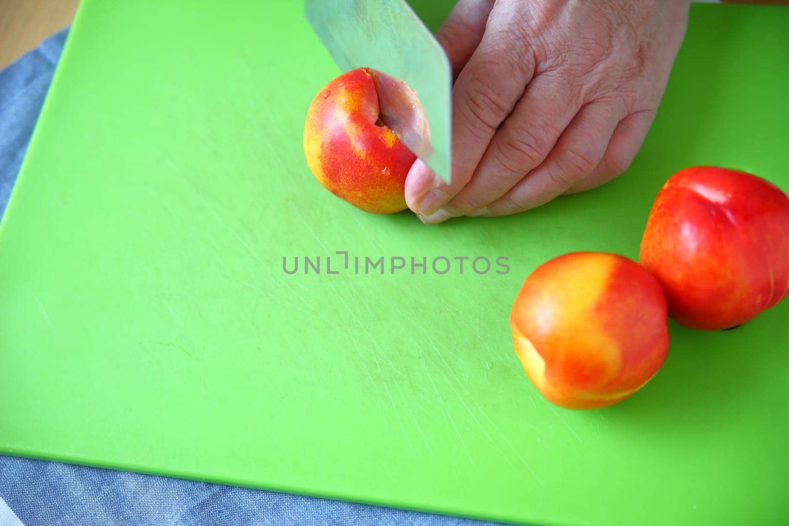 Older man slicing into a fresh nectarine on a green cutting board with room for text