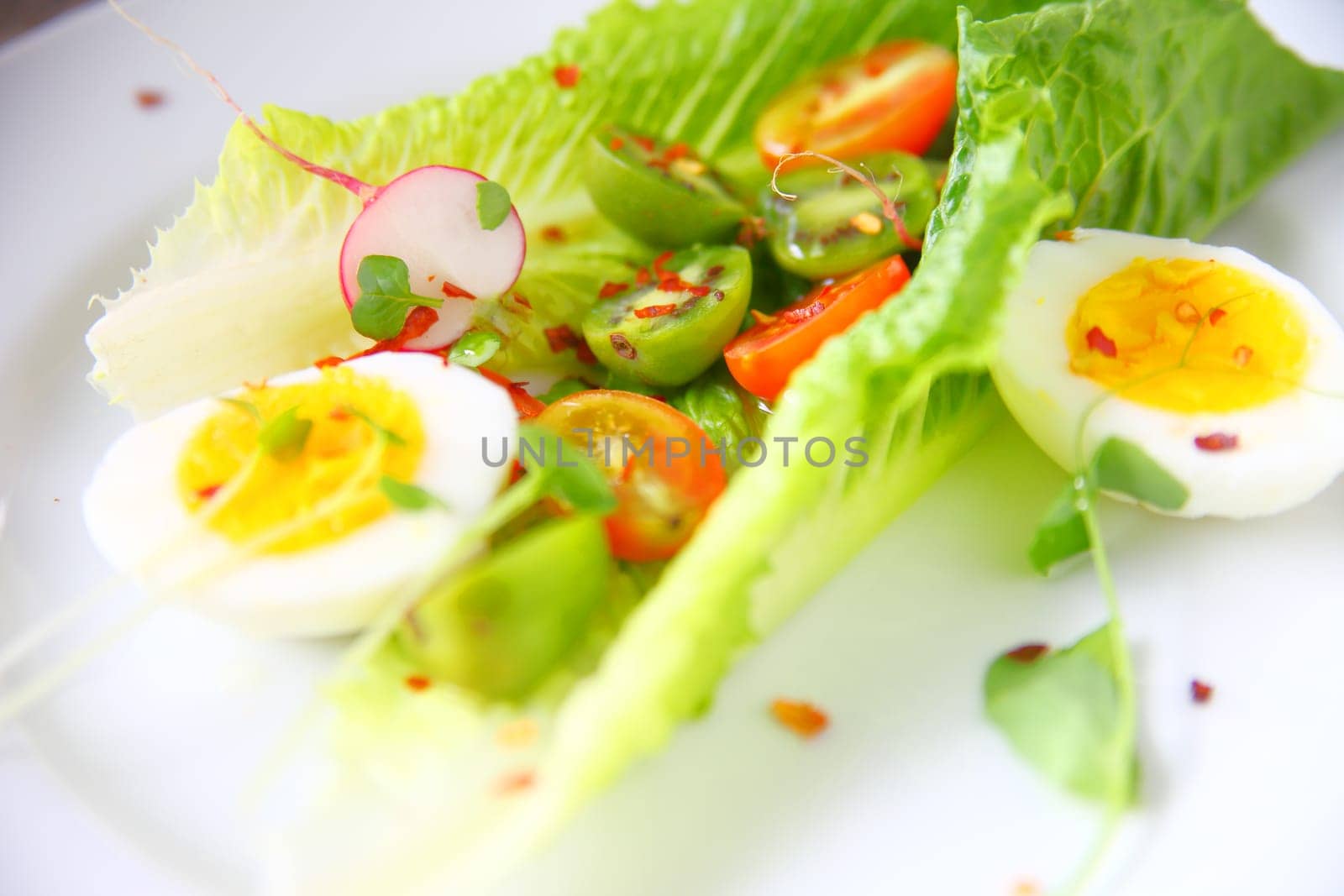 Closeup of romaine leaves with radishes, cherry tomatoes, baby kiwis, boiled eggs and chili pepper flakes