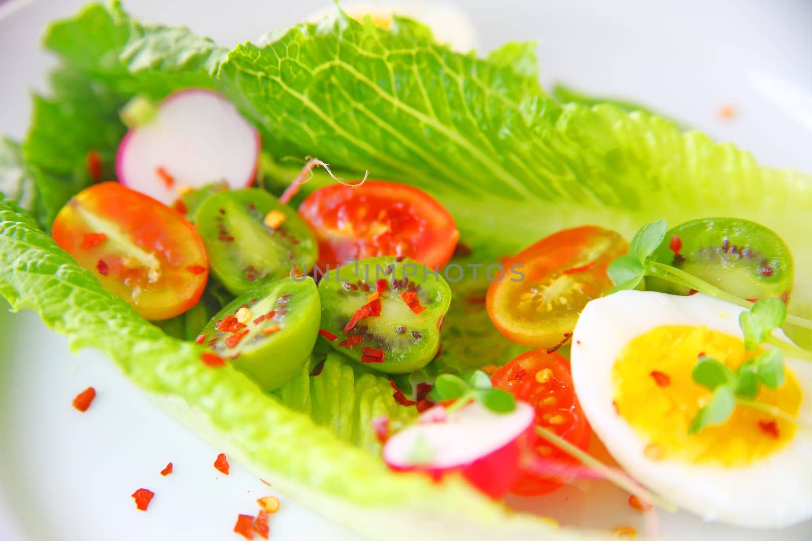 Salad of romaine leaves, boiled egg, cherry tomatoes, radishes and baby kiwi fruit with red pepper flakes