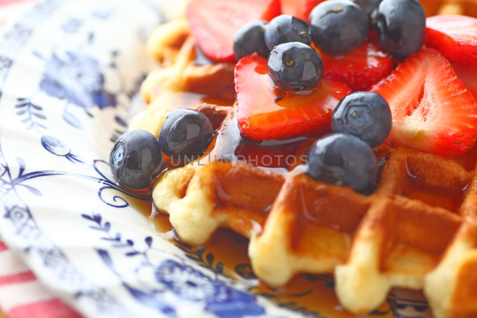 Closeup of homemade waffle with fresh strawberries and blueberries with syrup on a decorative plate