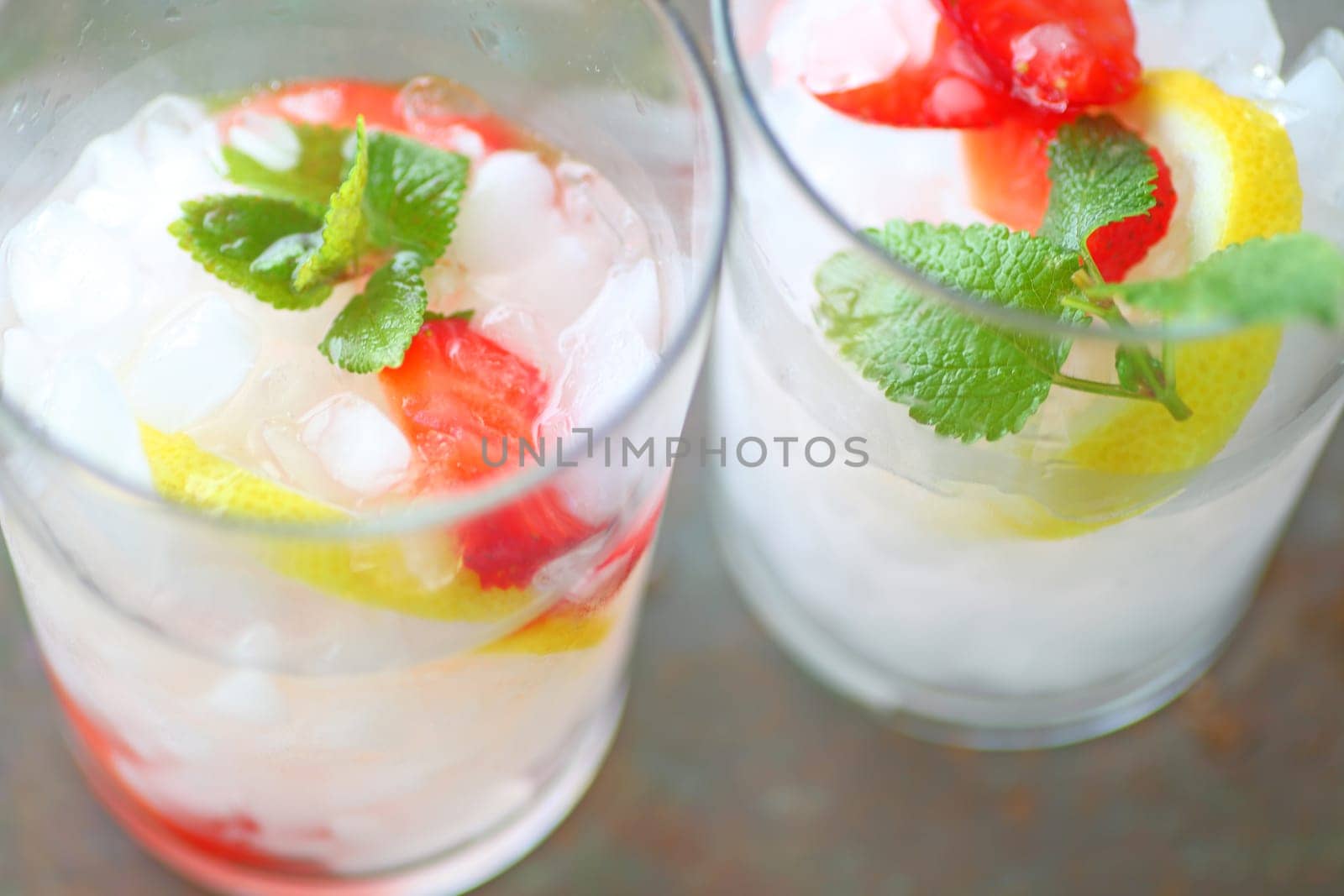 Overhead of two glasses of fruit-infused water with crushed ice, strawberries, lemon and mint