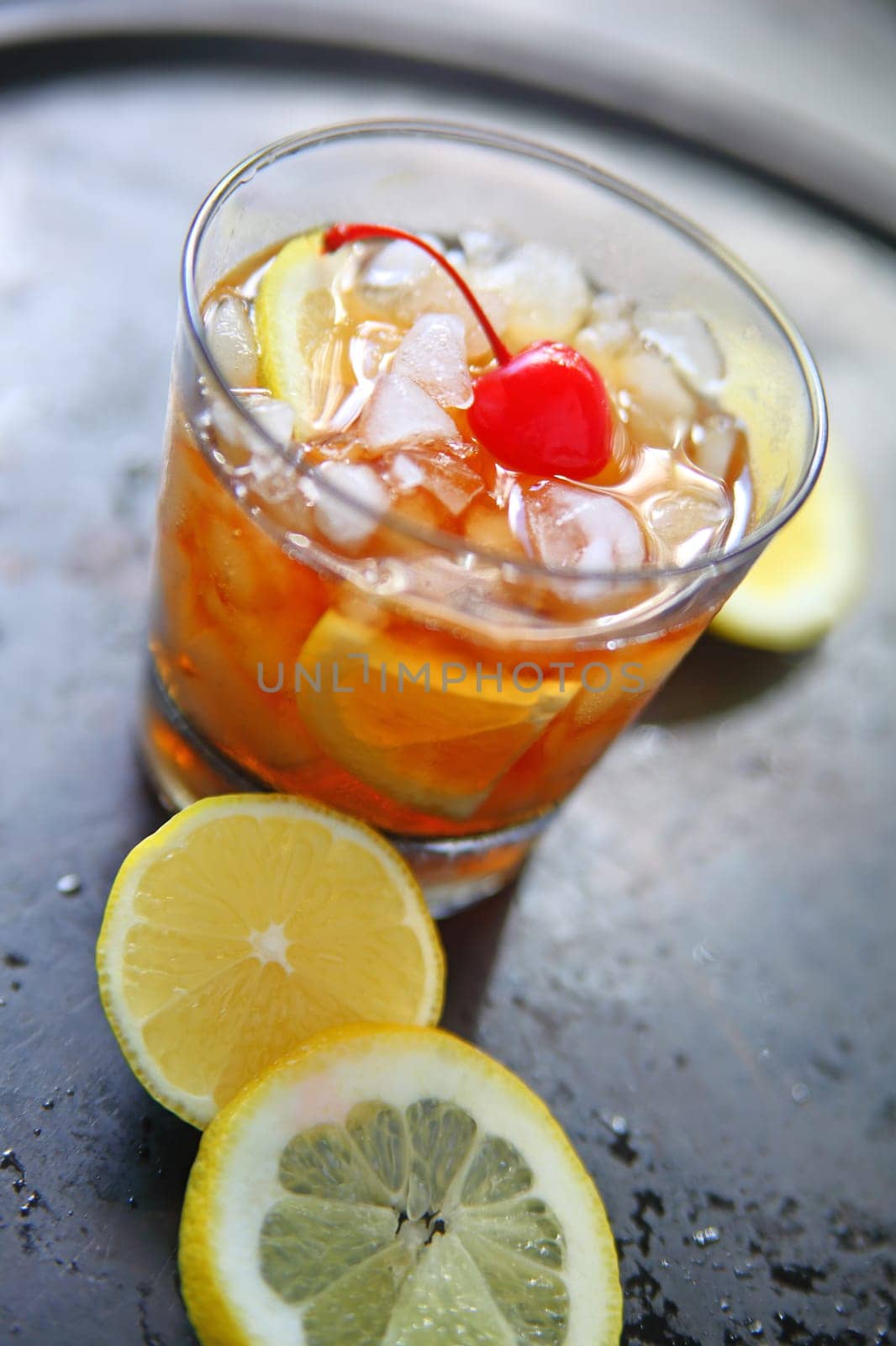 Whiskey sour cocktail with crushed ice, lemon and a maraschino cherry on a tray with lemon slices