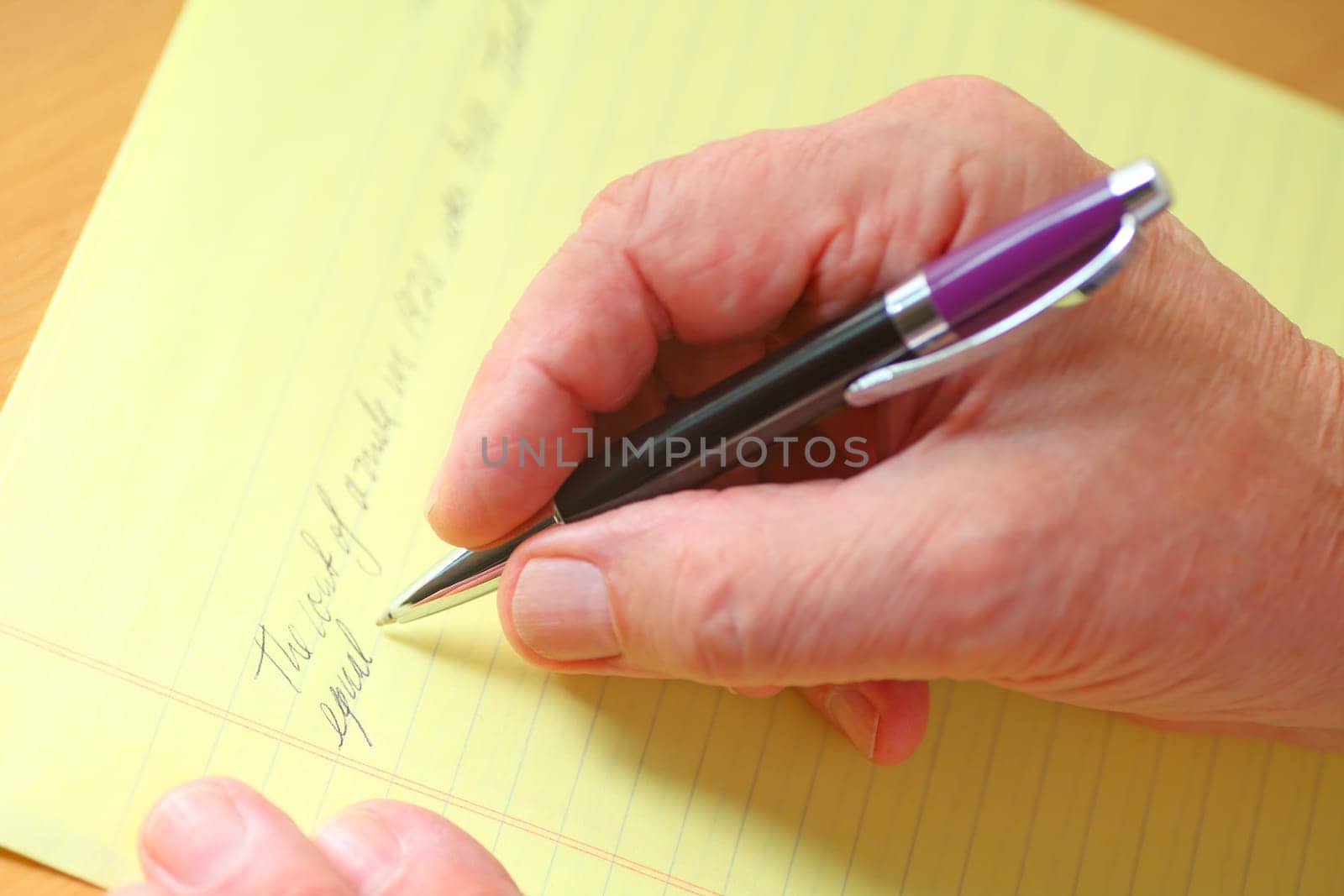 Older man writes in cursive on a ruled yellow pad of paper