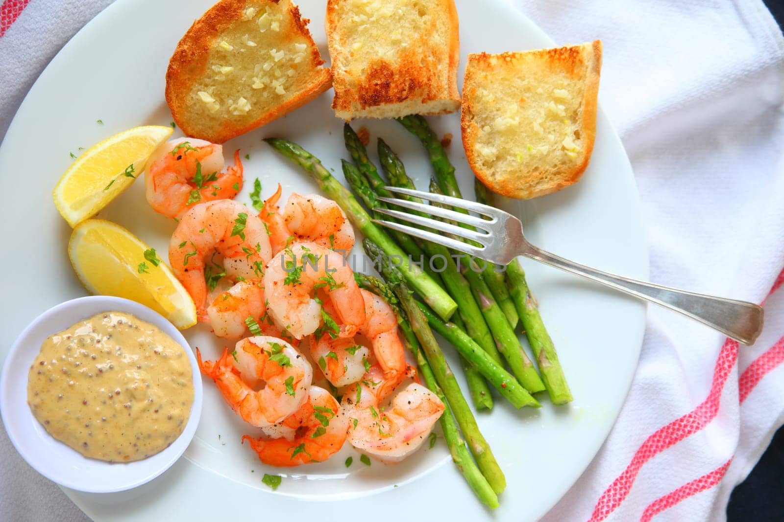 Overhead view of shrimp with asparagus and garlic bread with lemon and a tangy dipping sauce