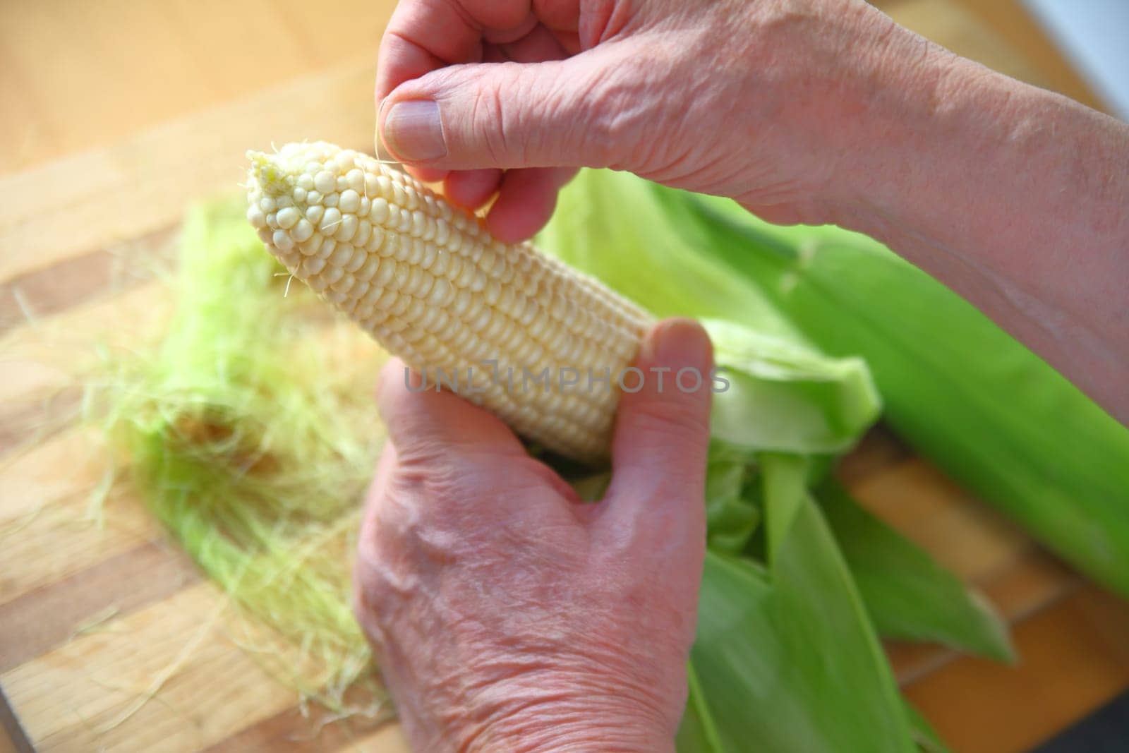Older man removing corn silk from an ear of white corn