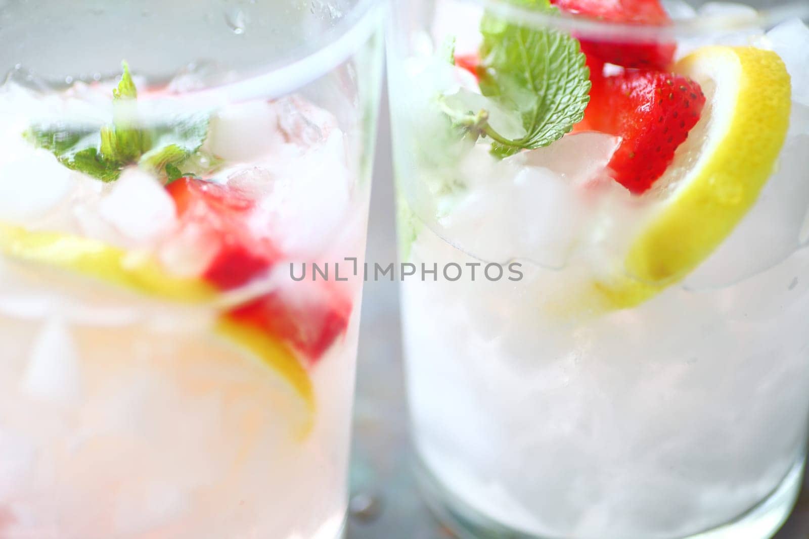 Closeup of two glassses of fruit-infused water with fresh strawberries, lemon slices and mint leaves