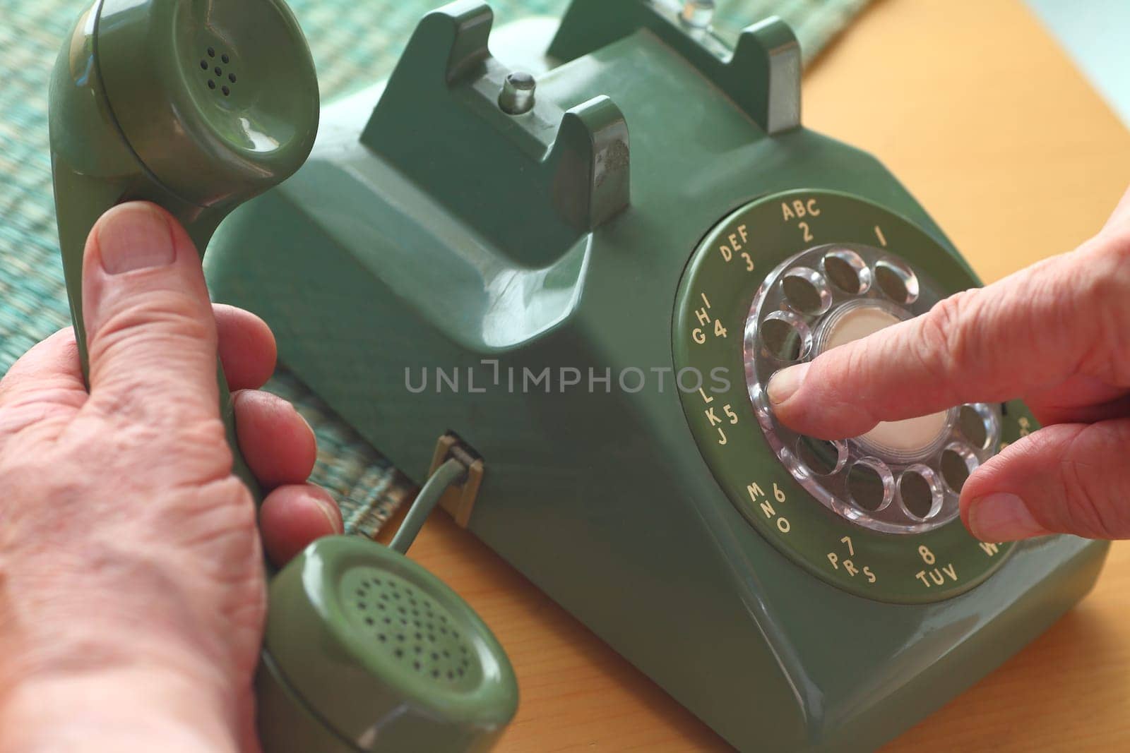 An older man dials a number on a vintage landline phone.