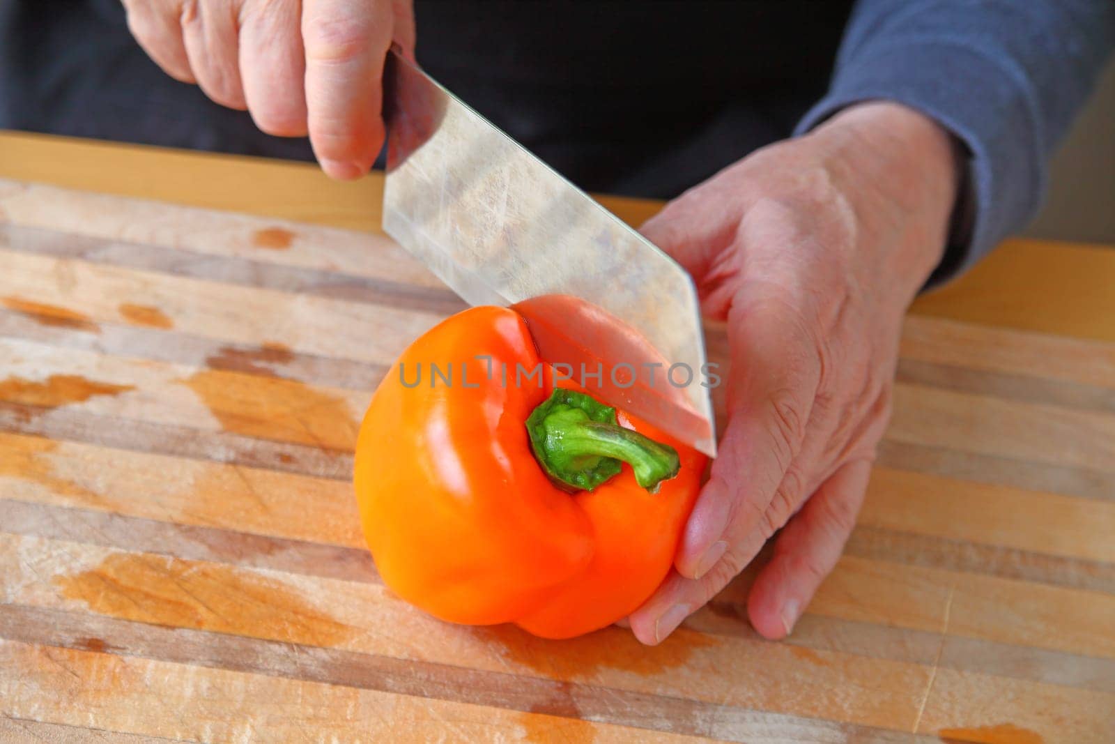 A man begins to cut into an orange bell pepper on a cutting board with copy space