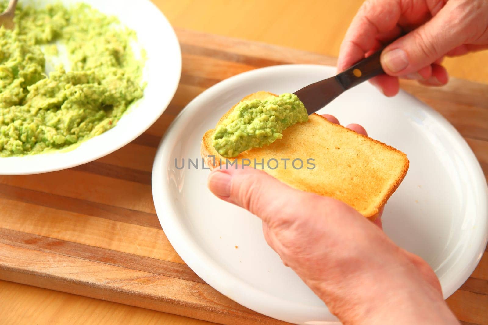A man spreads mashed avocado on a slice of brioche toast.