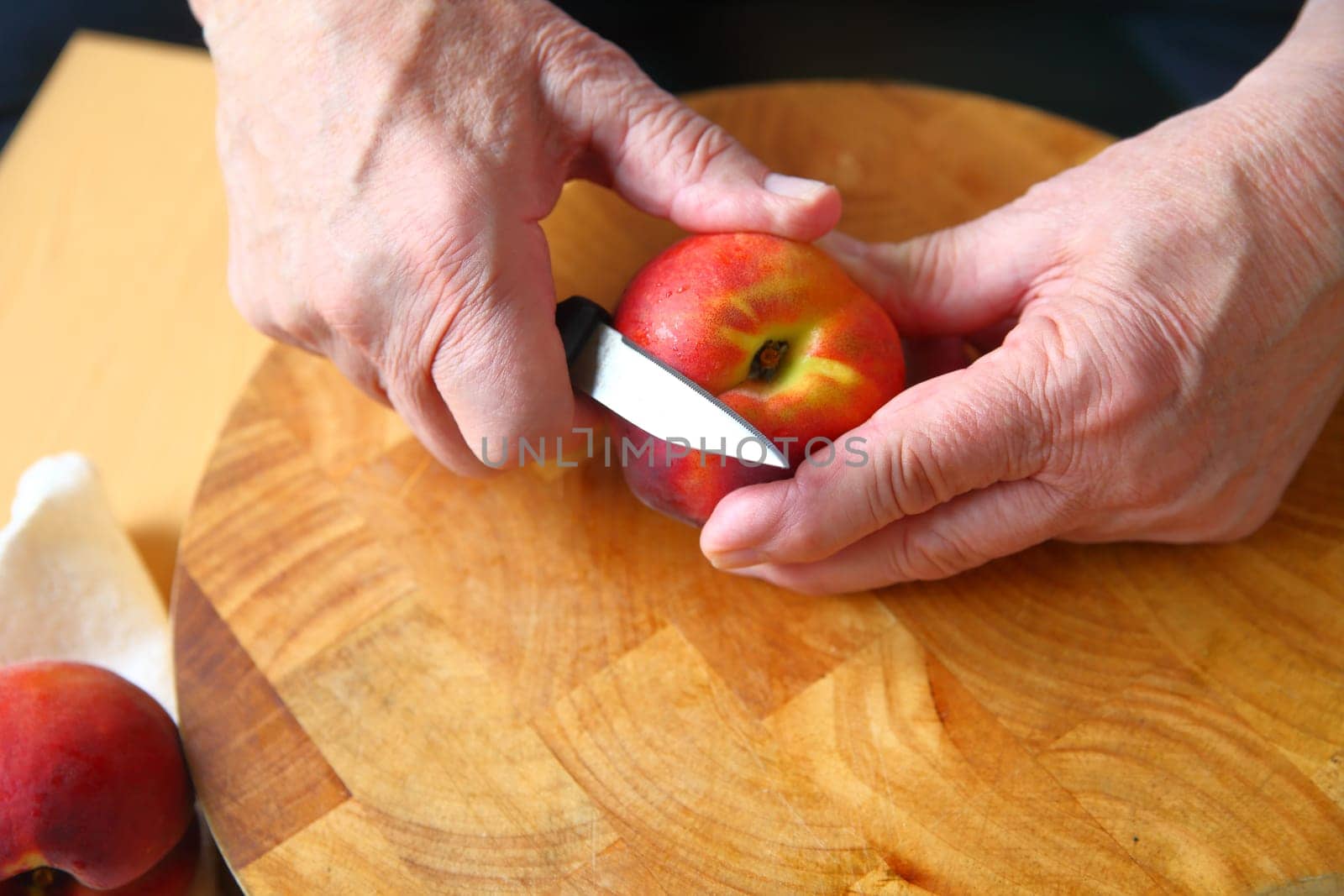 A man uses a paring knife to peel a fresh peach over a wood cutting board
