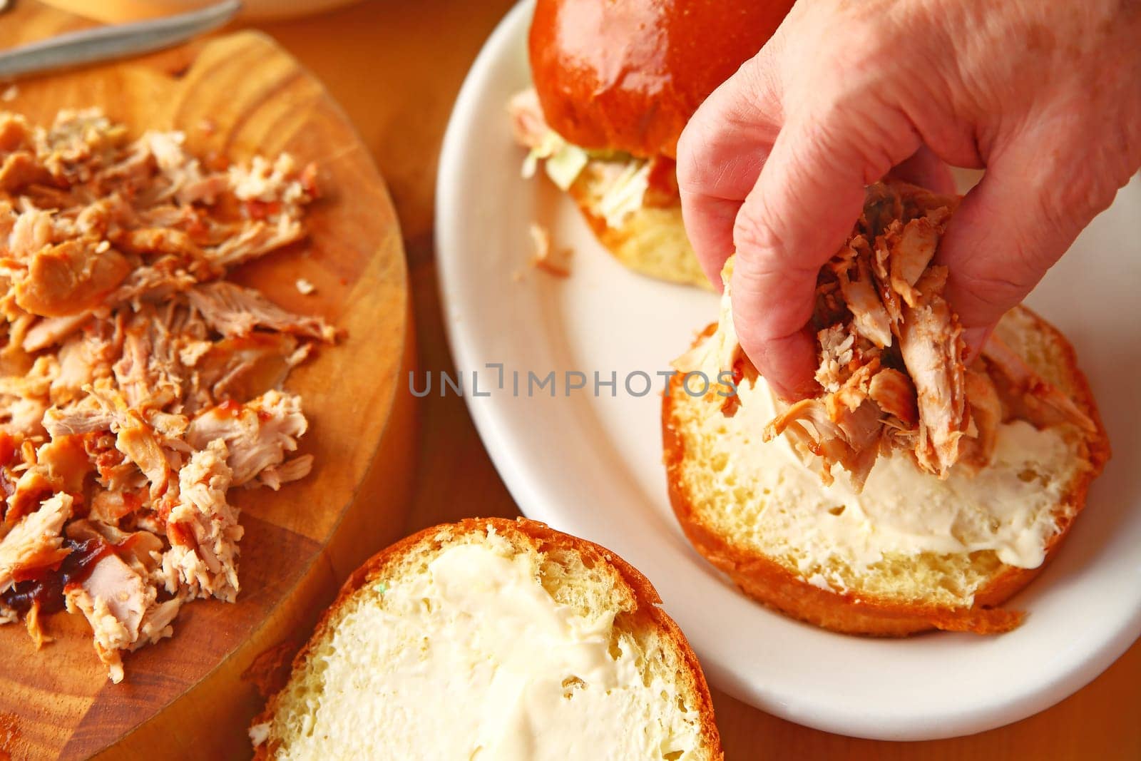 A man puts homemade pulled chicken on a brioche bun