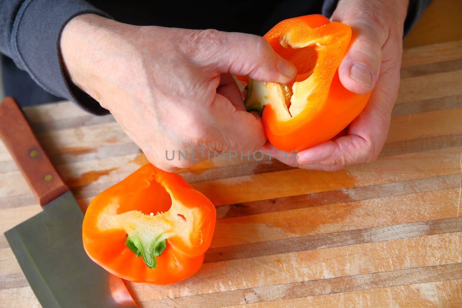 A man removes seeds from an orange-colored bell pepper over a cutting board with copy space