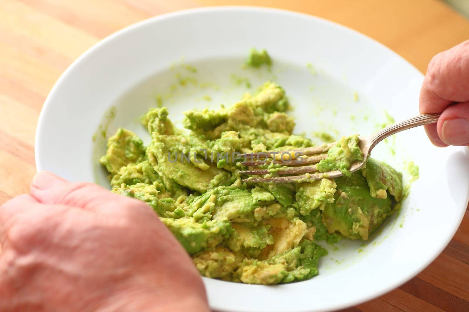Older man mashes an avocado using a fork point of view