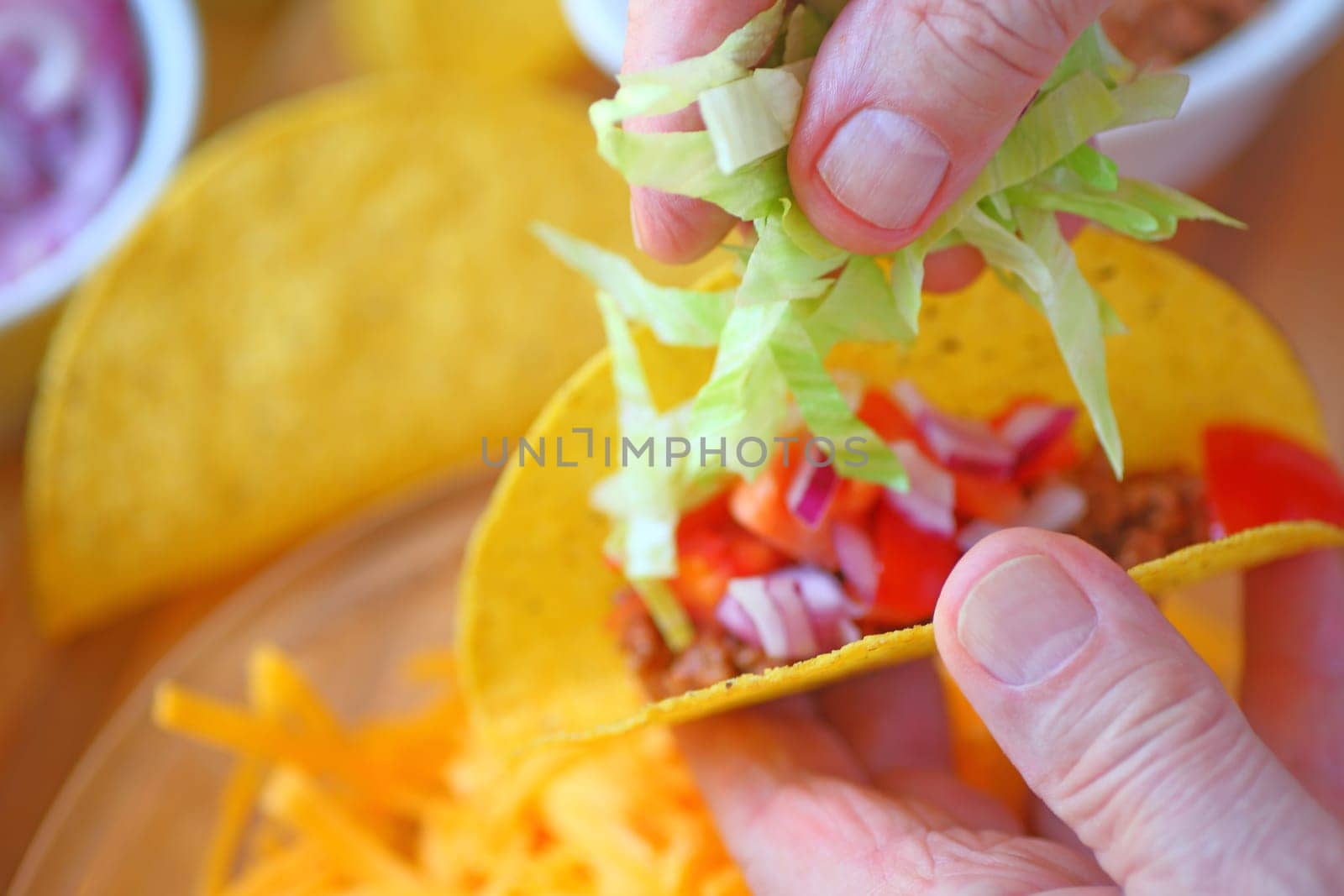 A man adds shredded lettuce to a homemade taco closeup