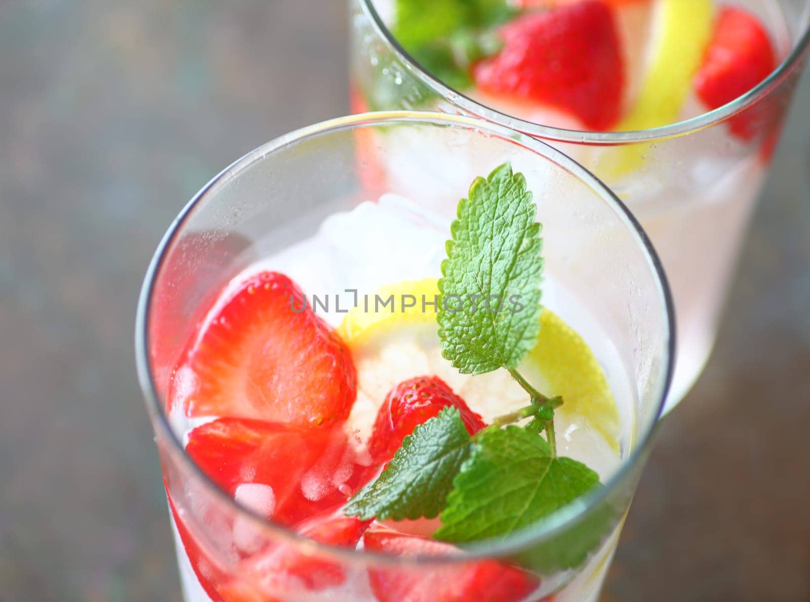 Two glasses of fruit water with fresh strawberries, lemon and mint over crushed ice