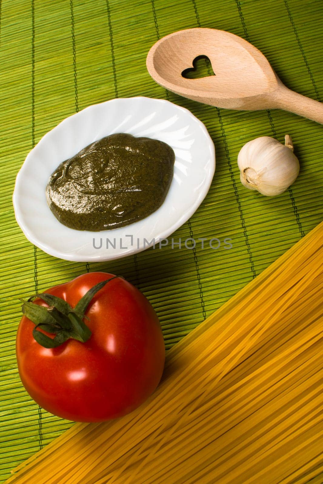 Italian food ingredients and a wooden spoon are on green background.