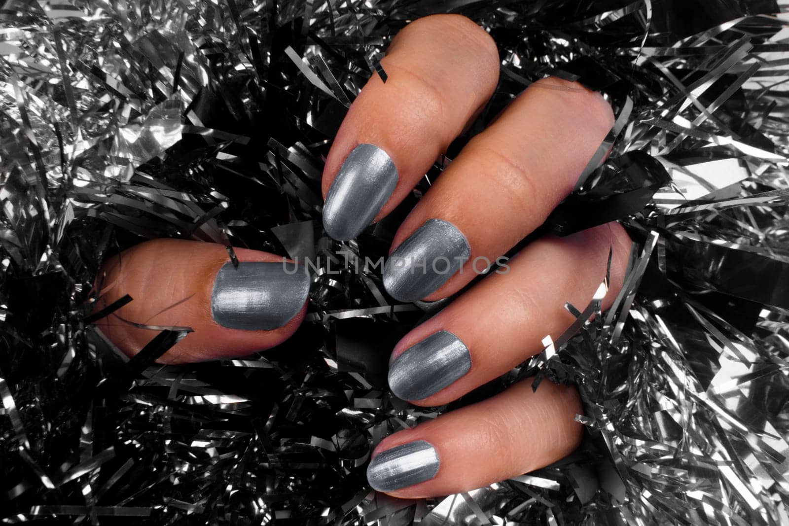Female hand with gray nails on black and silver texture background.