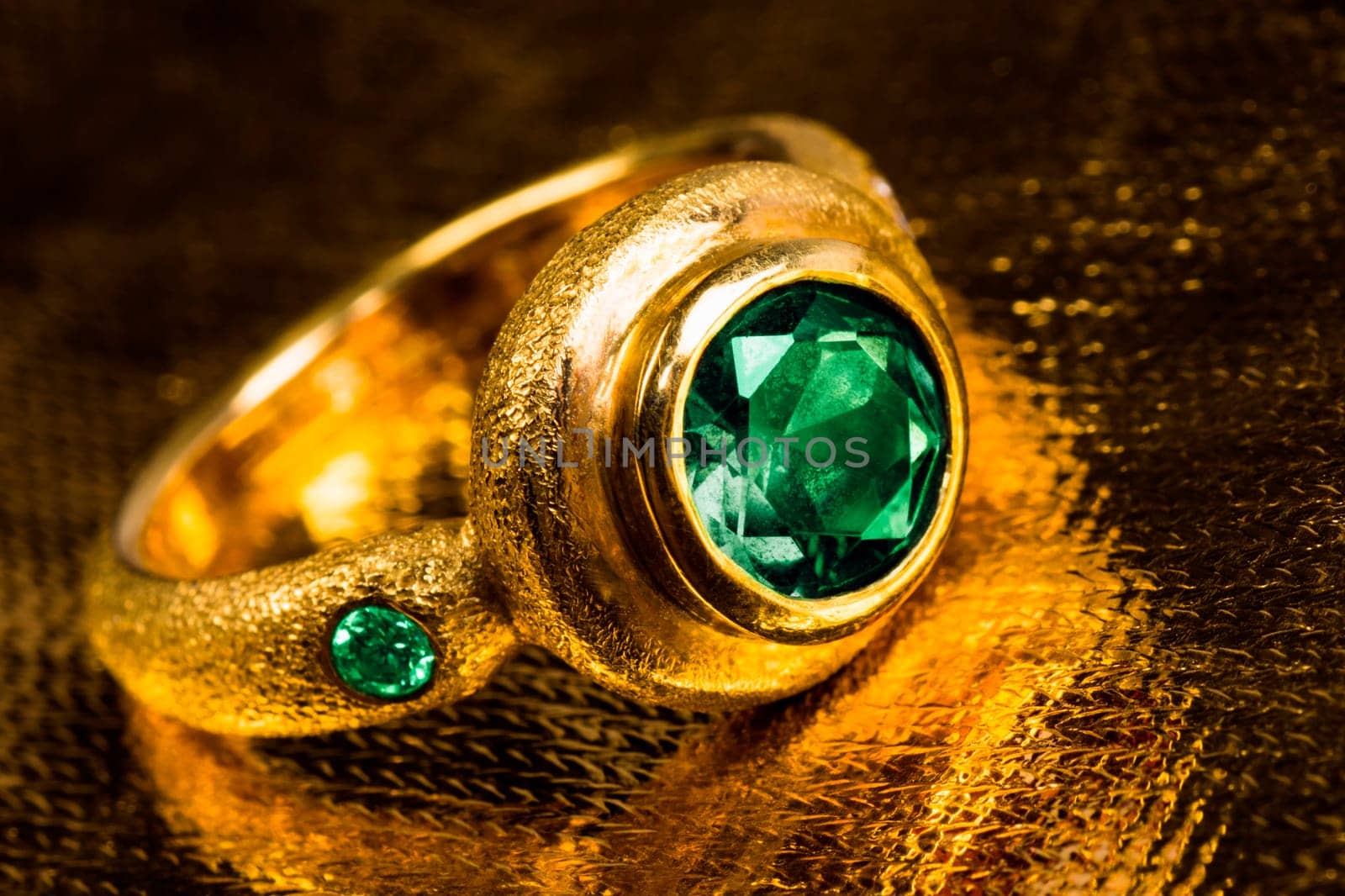 Gold ring with emerald or green gem is on golden background.