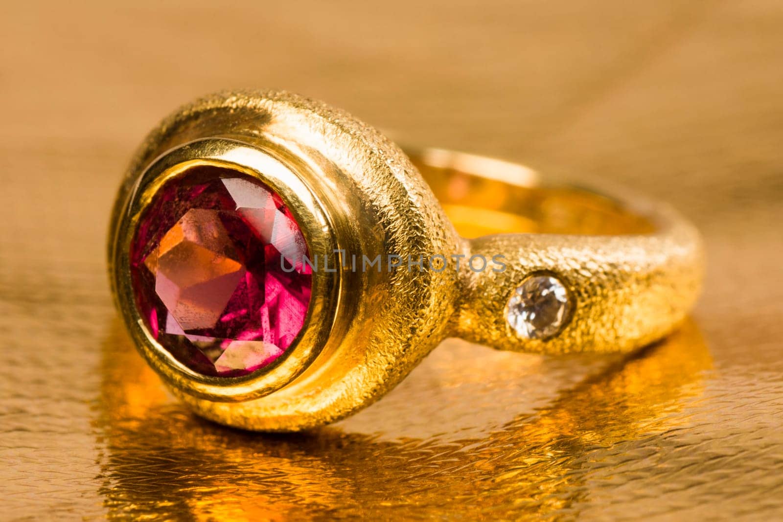 Gold ring with pink gem on golden background.