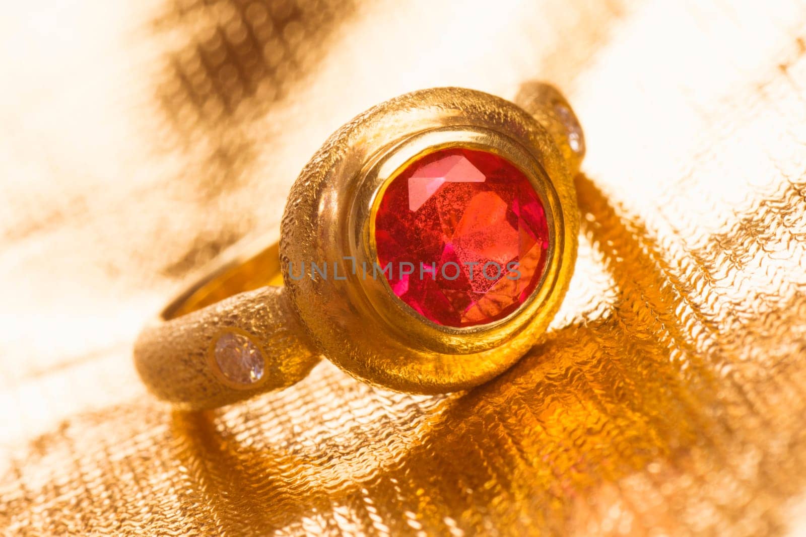 Gold ring with red gem is on golden background.