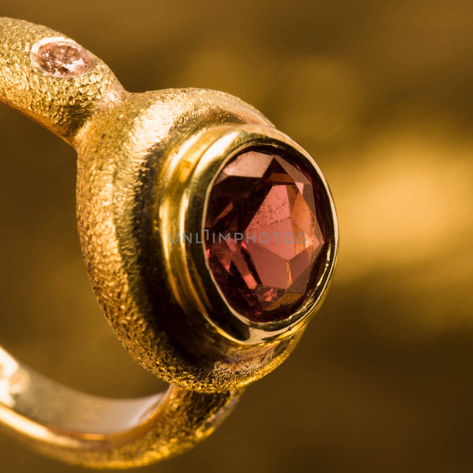 Gold ring with gem is on golden background.