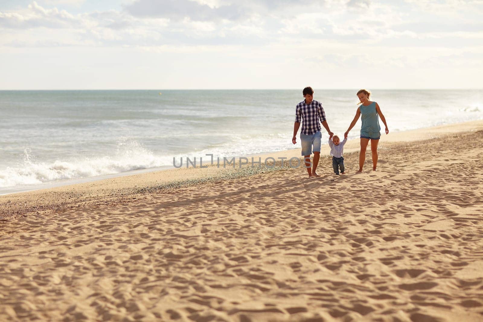 Mother and father with their toddler son walking together on a quiet beach