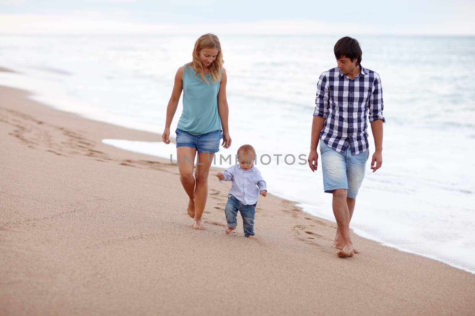 Young couple taking a seaside walk with their toddler