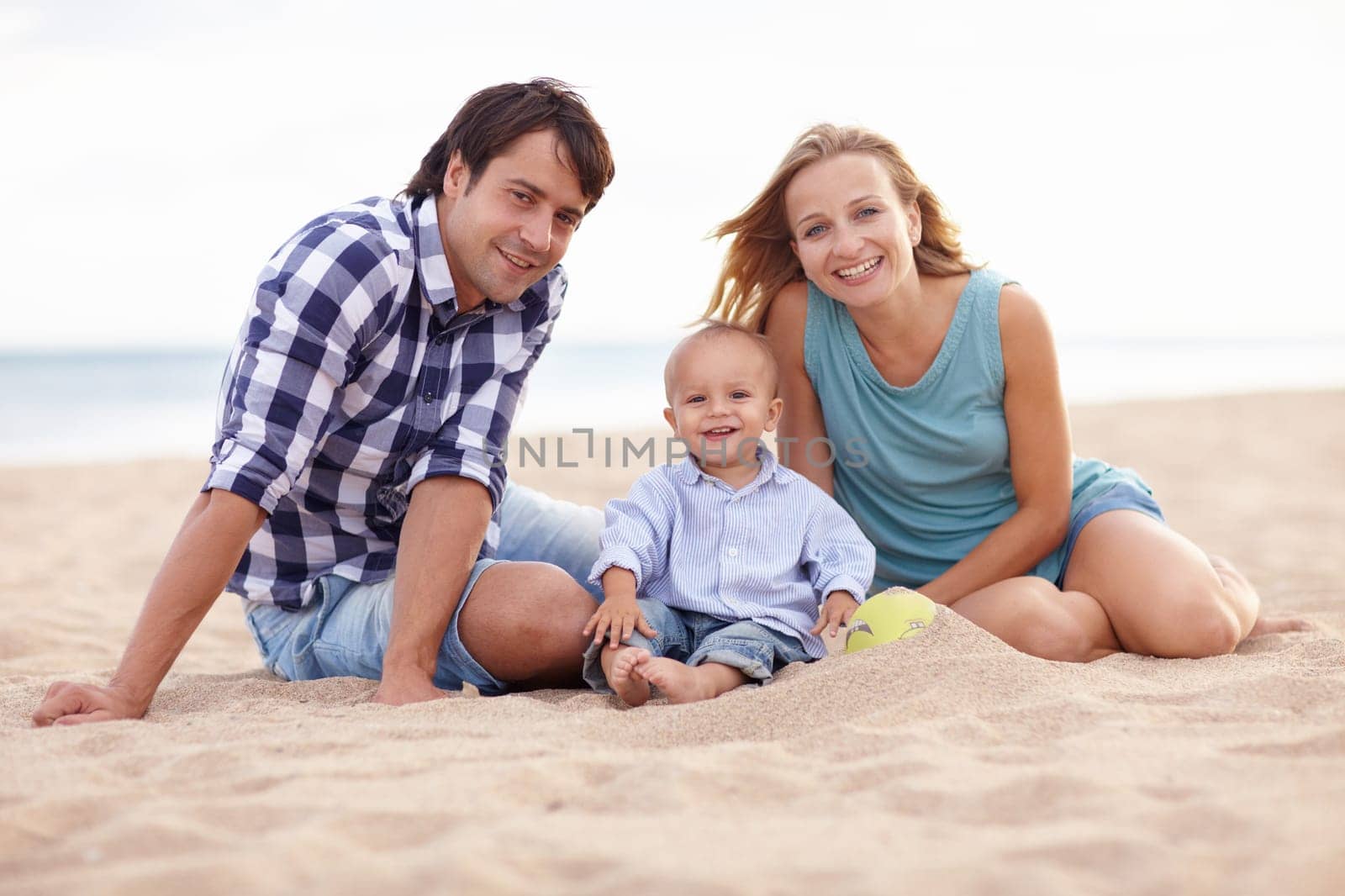 Portrait of two parents and their toddler playing together in the sand at the beach