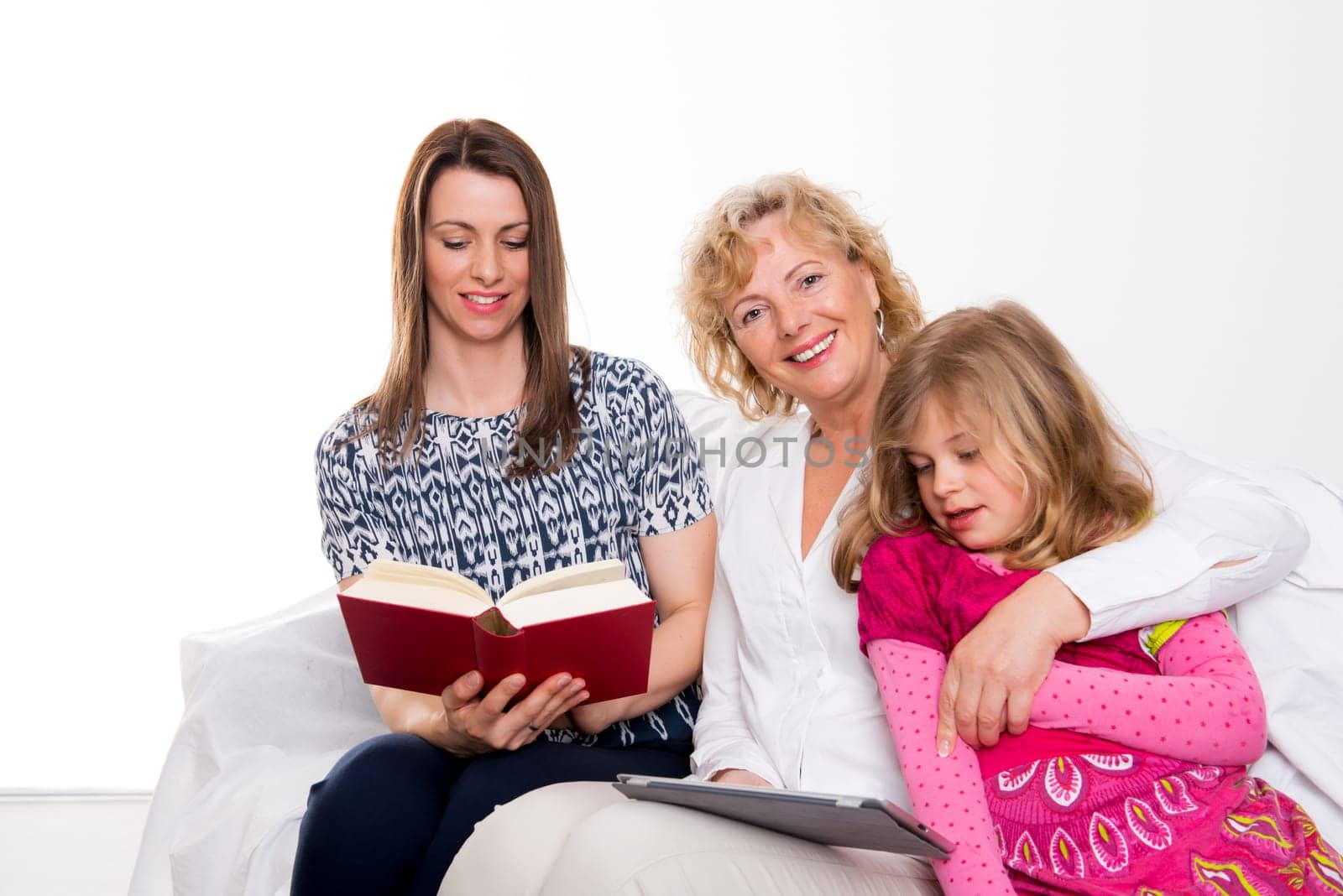 woman with daughter and grandchild together reading in book and tablet PC in front of white background