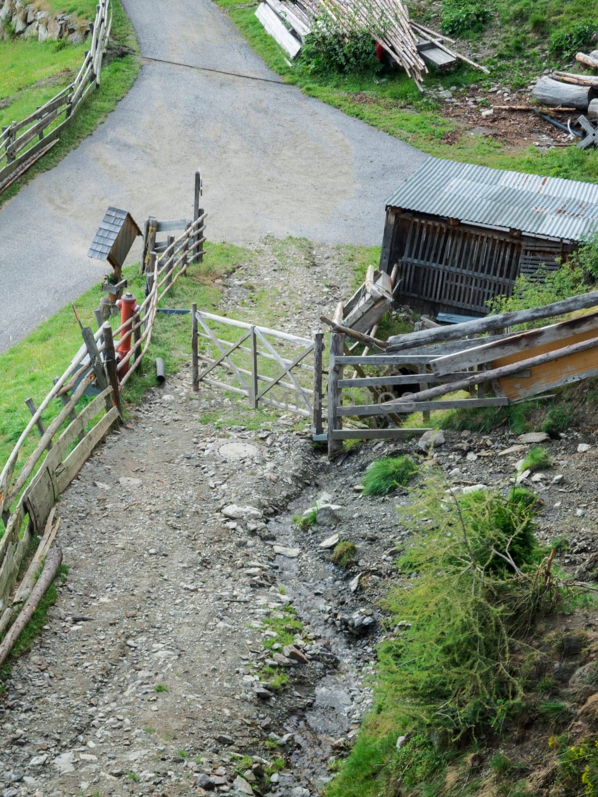 Elevated view of a fork in the path at a mountain farm with board fences and piles of wood in South Tyrol near the city of Merano.