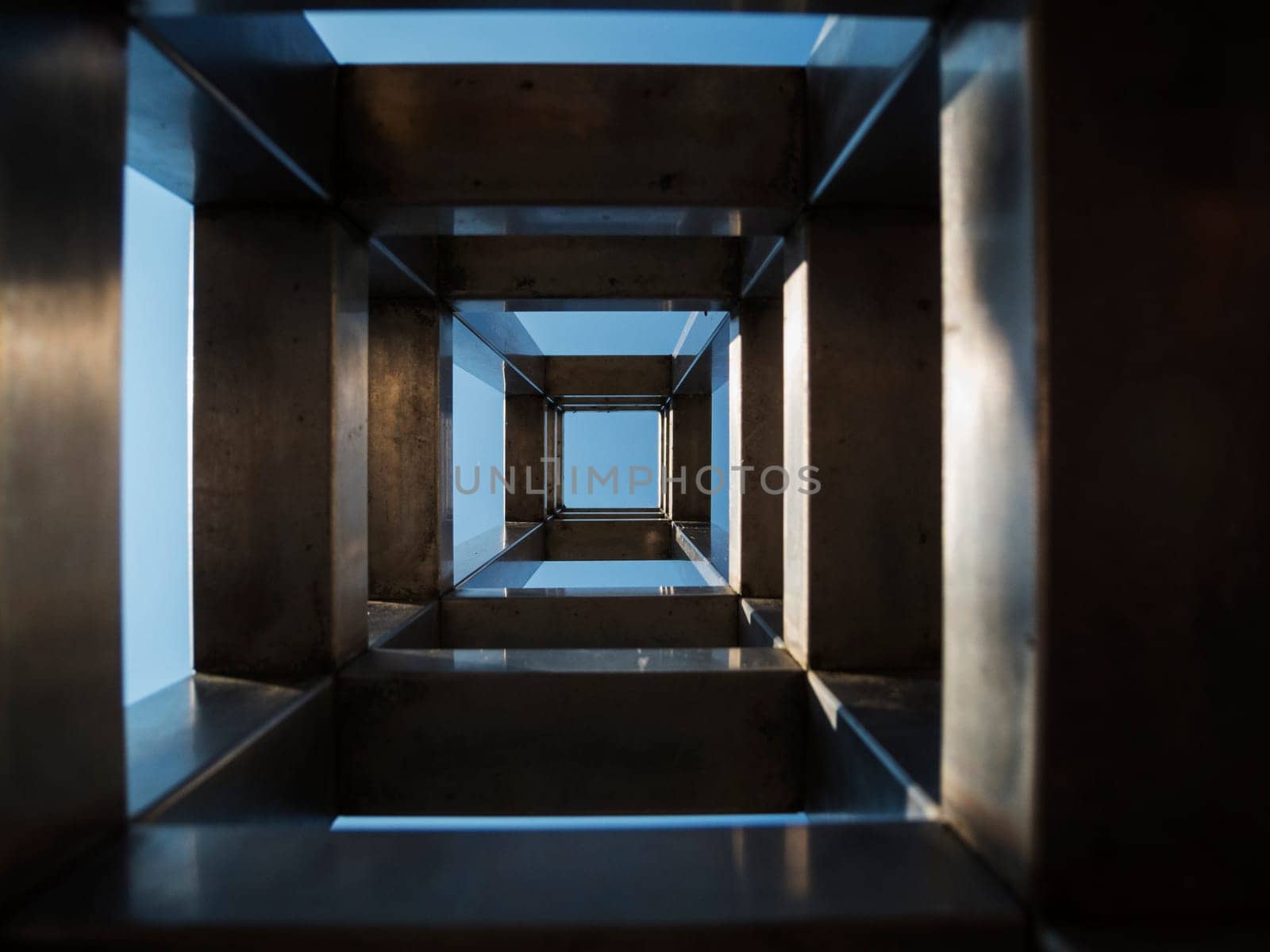 Repetitive square shapes inside a stainless steel column in front of a blue sky.