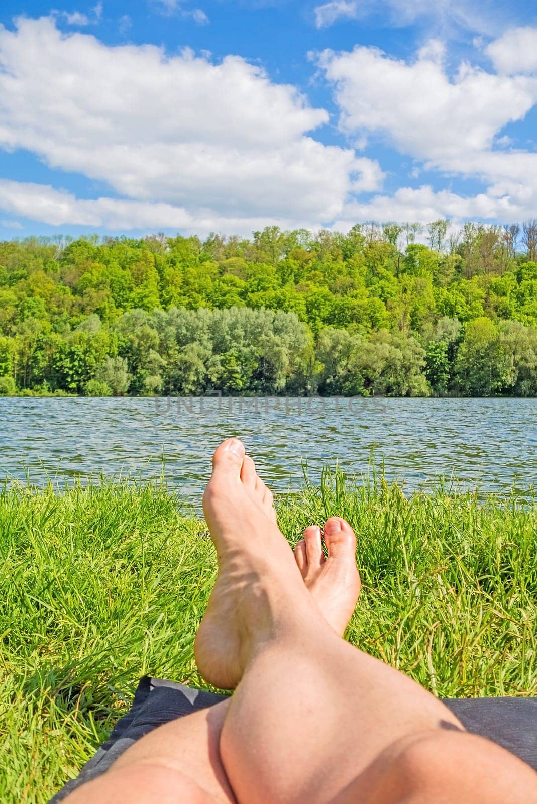 male feet at lake - man relaxing at lake on camping mat - green forest / trees in background