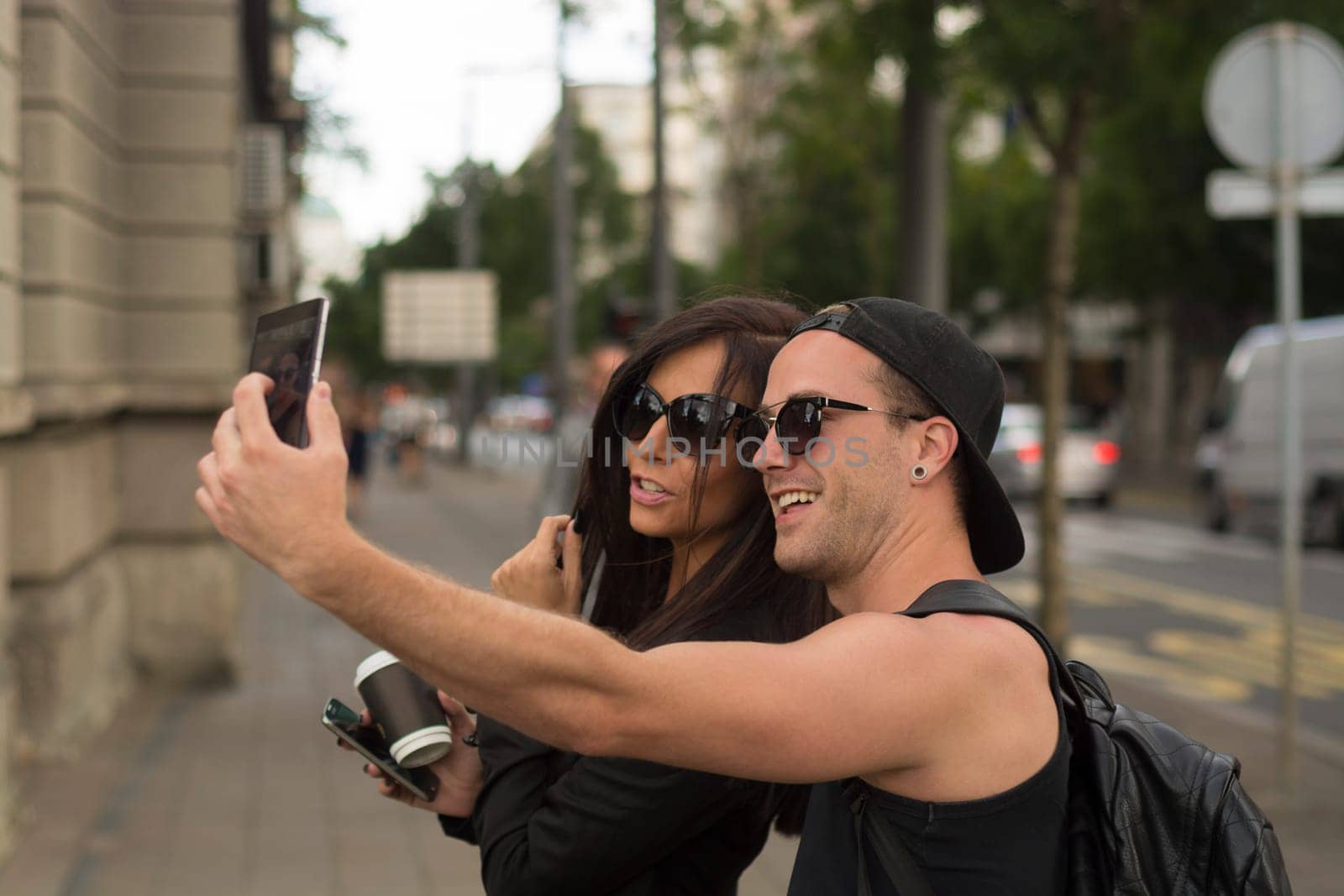 Cheerful friends taking photos of themselves on smart phone, urban city outdoor scene, selective focus