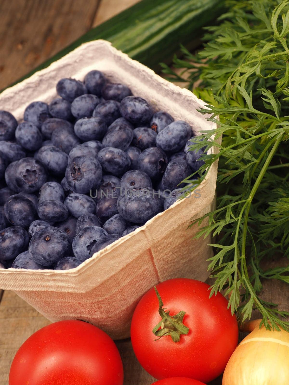 Freh fruits and vegetables, blueberries with tomatoes, carrots and onions on a rustic table